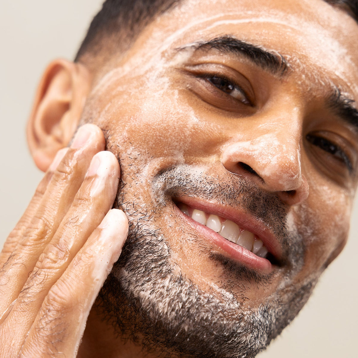 Close-up of man applying PAPATUI Hydrating Facial Cleanser to his face against a neutral background