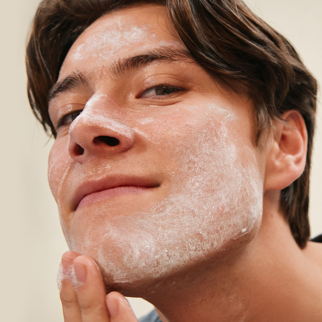 Man applying a white cream to his face against a neutral background