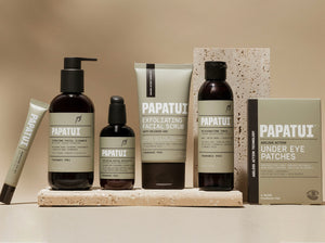 This image contains Papatui's full facial care line up on a neutral stone, beige background. From the left to right the product line up starts with Papatui Awakening Men's Eye Gel Rollerball, Unscented 0.5 oz, Papatui Hydrating Men's Facial Cleanser, Unscented 8 oz, Papatui Restoring Men's Facial Moisturizer, Unscented 3.3 oz, Papatui Men's Exfoliating Facial Scrub, Unscented 4 oz, Papatui Rejuvenating Men's Facial Toner, Unscented, 6 oz, and lastly Papatui Ageless Action Technology Men's Under Eye Patches.