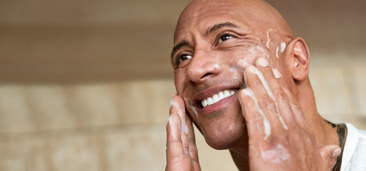 Dwayne "The Rock" Johnson applying PAPATUI Facial Cleanser to his face against a neutral background
