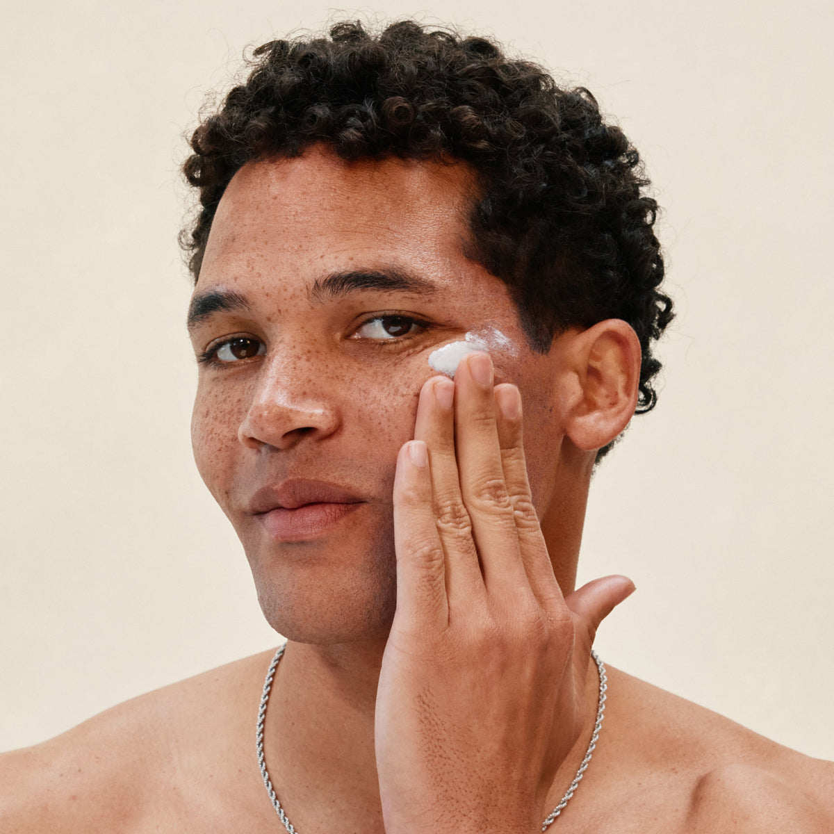 Man applying white cream to his face against a neutral background