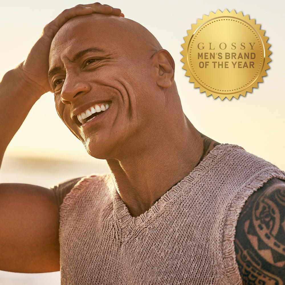 Dwayne "The Rock" Johnson smiling outdoors, with gold award badge that reads "Glossy Men's Brand of the Year"