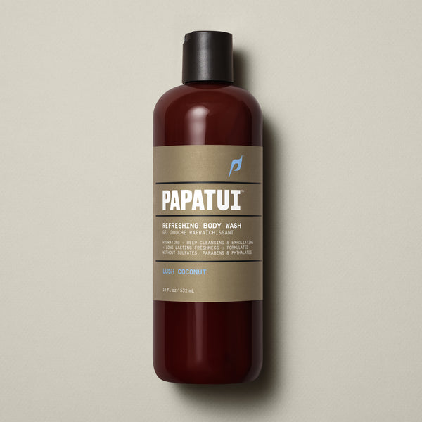 PAPATUI™ Refreshing Body Wash 18 fl oz in Lush Coconut scent. The product is presented in an amber bottle with a beige minimalist label and black flip cap. Key label highlights include hydrating and exfoliating formula with long-lasting freshness. Claims sulfate-free, paraben-free, phthalate-free formulation. Neutral beige background.