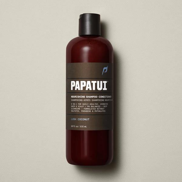 PAPATUI™ Nourishing Shampoo + Conditioner 18 fl oz in Lush Coconut scent. The product is contained in a sleek amber bottle with a dark brown minimalist label and black flip-top cap. Label highlights include 2-in-1 hydration, pH balanced formula, deep cleansing, and sulfate-free, paraben-free, phthalate-free properties. Set on a soft beige background.
