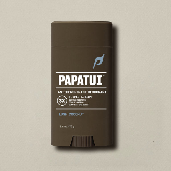 PAPATUI™ Antiperspirant Deodorant 2.6 oz in Lush Coconut scent. The product is housed in a dark brown stick with a minimalist beige and white label and light blue PAPATUI™ logo. Callouts on the label highlight triple-action benefits: blocks moisture, odor fighting, and long-lasting scent. Positioned against a neutral beige background.