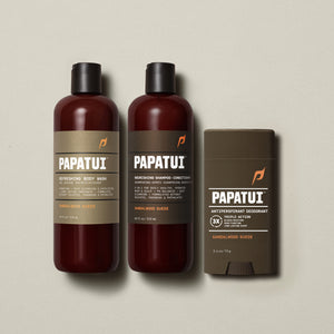 PAPATUI™ Body Care Bundle in Sandalwood Suede scent, featuring the full set: Refreshing Body Wash 18 fl oz, Nourishing Shampoo + Conditioner 18 fl oz, and Antiperspirant Deodorant 2.6 oz. Products are arranged on a soft beige background, showcasing consistent amber and brown minimalist packaging with bold PAPATUI™ branding.