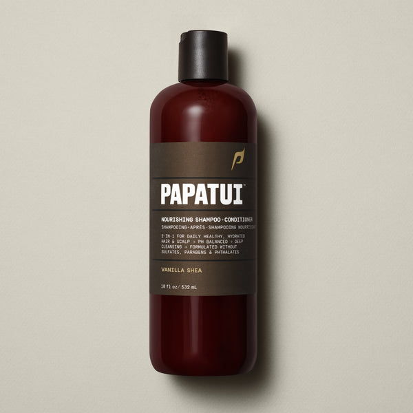PAPATUI™ Nourishing Shampoo + Conditioner 18 fl oz in Vanilla Shea scent. The product is contained in a sleek amber bottle with a dark brown minimalist label and black flip-top cap. Label highlights include 2-in-1 hydration, pH balanced formula, deep cleansing, and sulfate-free, paraben-free, phthalate-free properties. Set on a soft beige background.