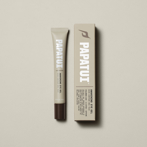 PAPATUI™ Awakening Eye Gel 0.5 fl oz revitalizing eye gel designed to reduce puffiness, brighten dark circles, and refresh tired eyes. Formulated with hyaluronic acid, tetrapeptides, and caffeine to hydrate, depuff, and energize the under-eye area. Features a cooling metal roll-on applicator for easy and soothing application. The image showcases the sleek beige tube alongside its matching box, both with bold white typography displaying the PAPATUI™ logo, emphasizing its modern and effective skincare formula