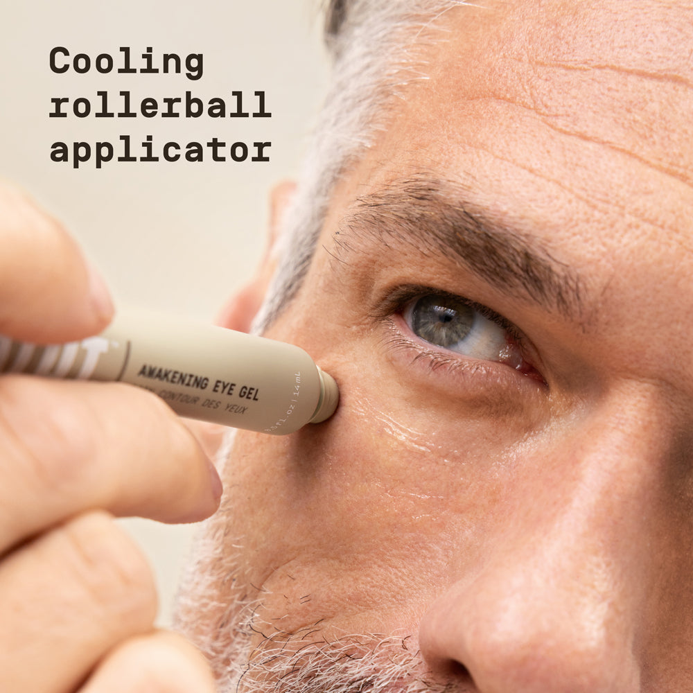 Close-up of man applying PAPATUI Awakening Eye Gel against a neutral background with text overlay that reads "Cooling rollerball applicator"