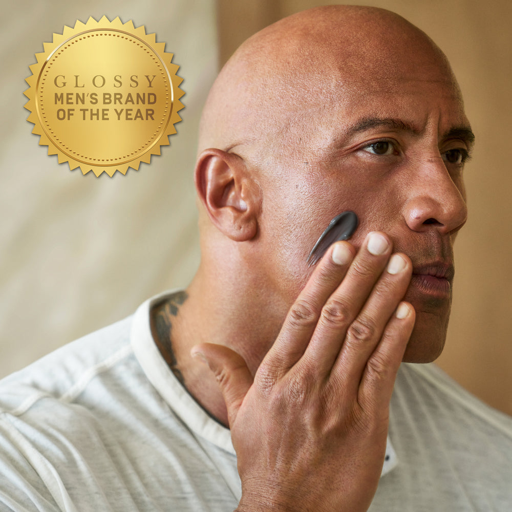 Dwayne "The Rock" Johnson applying PAPATUI Men’s Exfoliating Facial Scrub to his face against a neutral background with a gold award badge in the top left corner that reads "Glossy Men's Brand of the Year"