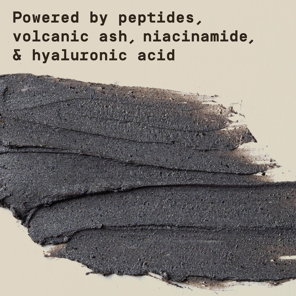 Close-up of PAPATUI Men’s Exfoliating Facial Scrub smeared on a neutral background with text overlay that reads "Powered by peptides, volcanic ash, niacinamide, & hyaluronic acid"