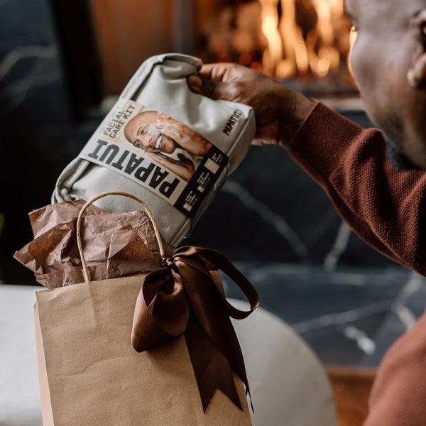 This image shows a man revealing the Papatui holiday gift set facial care dopp kit our of a gift back highlighting giftable men's care.
