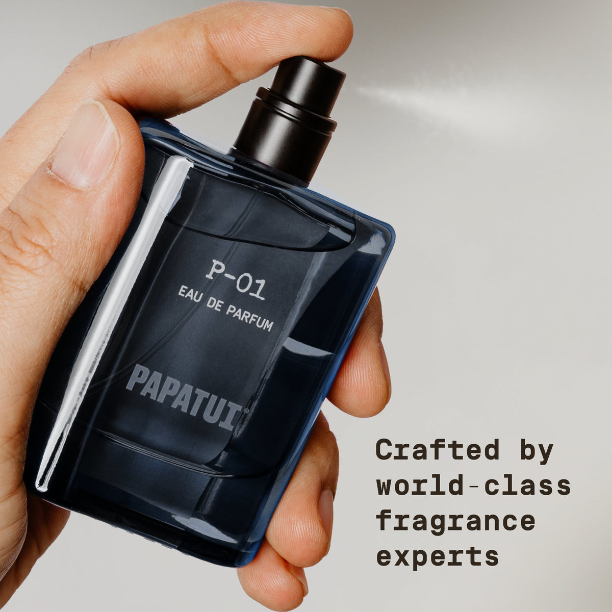 Hand holding a blue cologne bottle labeled 'P-01 Eau de Parfum' by PAPATUI against a neutral background with text overlay that reads "Crafted by world-class fragrance experts"
