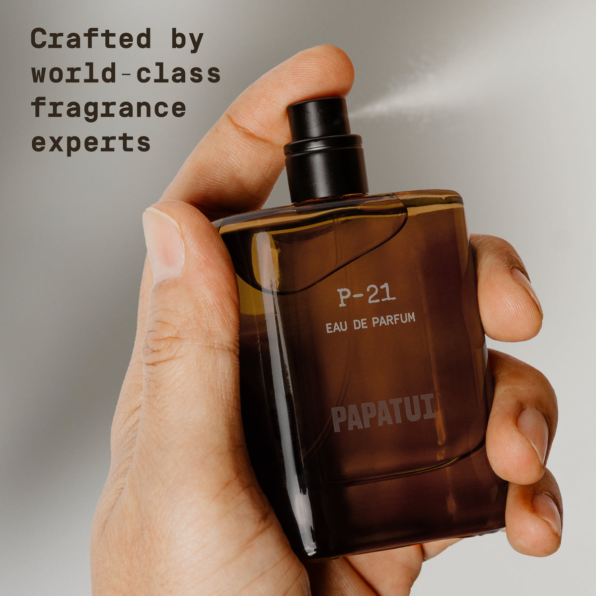Hand holding amber cologne bottle labeled 'P-21 Eau de Parfum' by 'PAPATUI' on a beige background with text overlay that reads "Crafted by world-class fragrance"