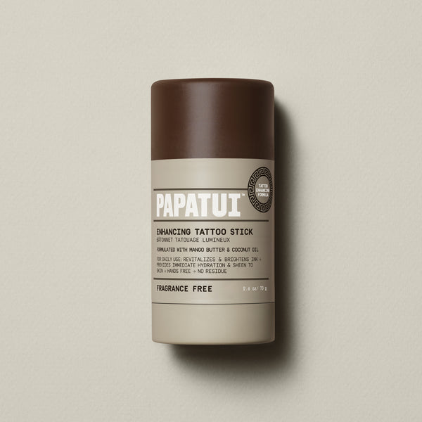 PAPATUI™ Enhancing Tattoo Stick in Fragrance Free, 2.6 oz. The product is housed in a dark brown stick with a minimalist beige and white label featuring the PAPATUI™ logo. Formulated with mango butter and coconut oil to hydrate and brighten tattoos.