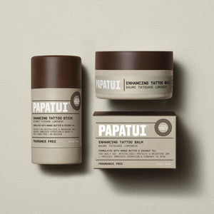 PAPATUI™ Tattoo Care Bundle including Enhancing Tattoo Stick 2.6 oz, Enhancing Tattoo Balm 2 fl oz jar, and its accompanying box. The full collection is presented on a neutral beige background. All products feature a cohesive minimalist design in matte beige and brown with bold PAPATUI™ branding.