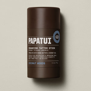 PAPATUI™ Enhancing Tattoo Stick Coconut Woods 2.6 oz stick standing alone on neutral background. Formulated with mango butter and coconut oil to hydrate skin and brighten tattoo ink with a signature coconut woods scent.