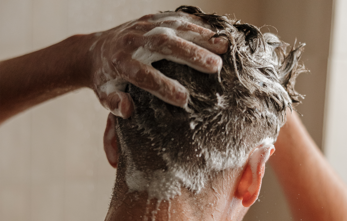 Man washing their hair with soapy hands against a neutral background