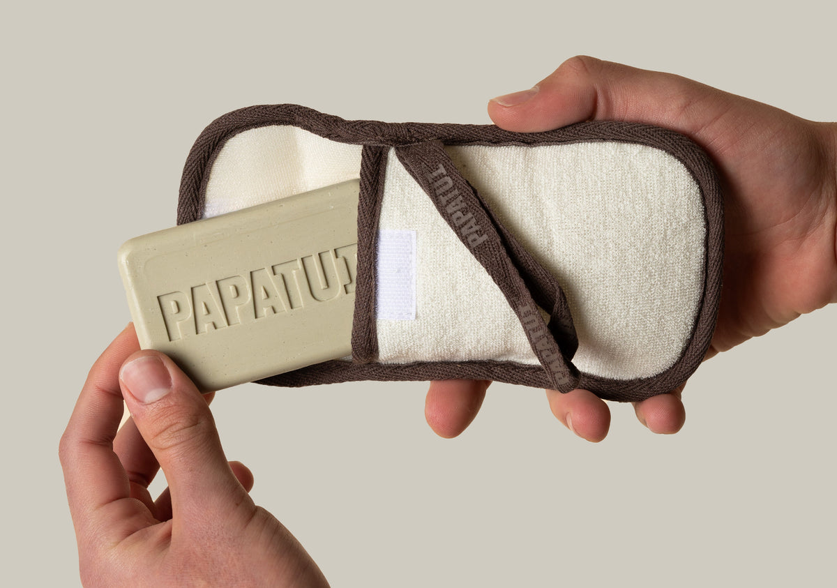 Hand holding PAPATUI Exfoliating Body Scrubber and Big Bar Soap against a neutral background