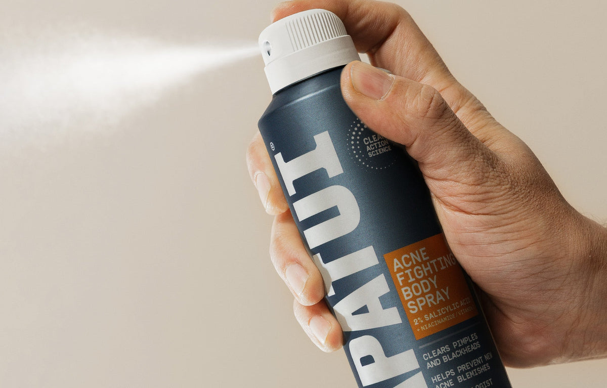 Hand spraying PAPATUI Acne Fighting Body Spray against a neutral background