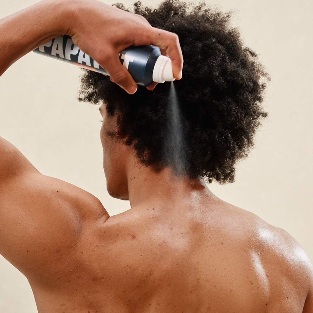 Man spraying PAPATUI Acne Fighting Body Spray to his back against a neutral background