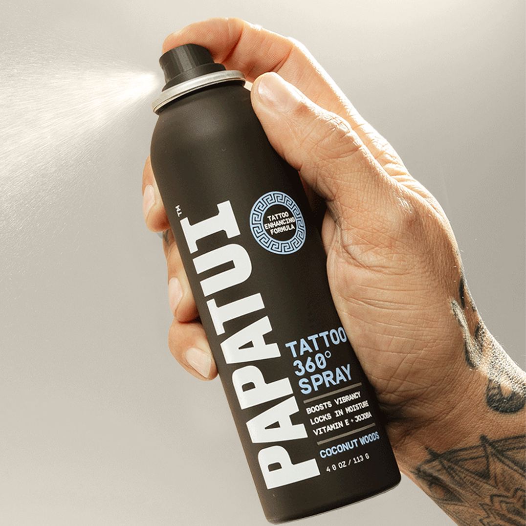 Hand holding a black PAPATUI Tattoo Spray can against a neutral background