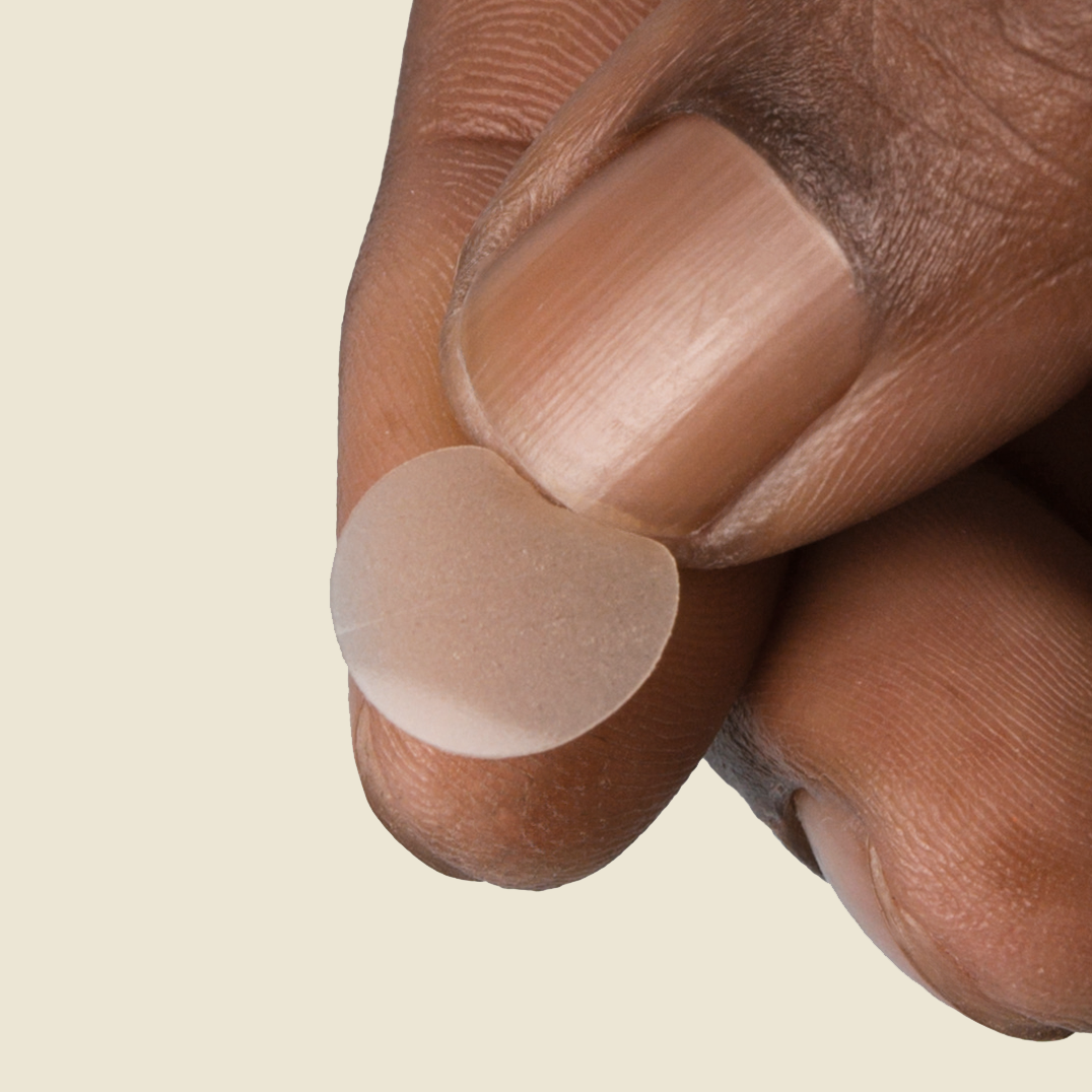 Close-up of fingers holding a PAPATUI Pimple Patch against a neutral background