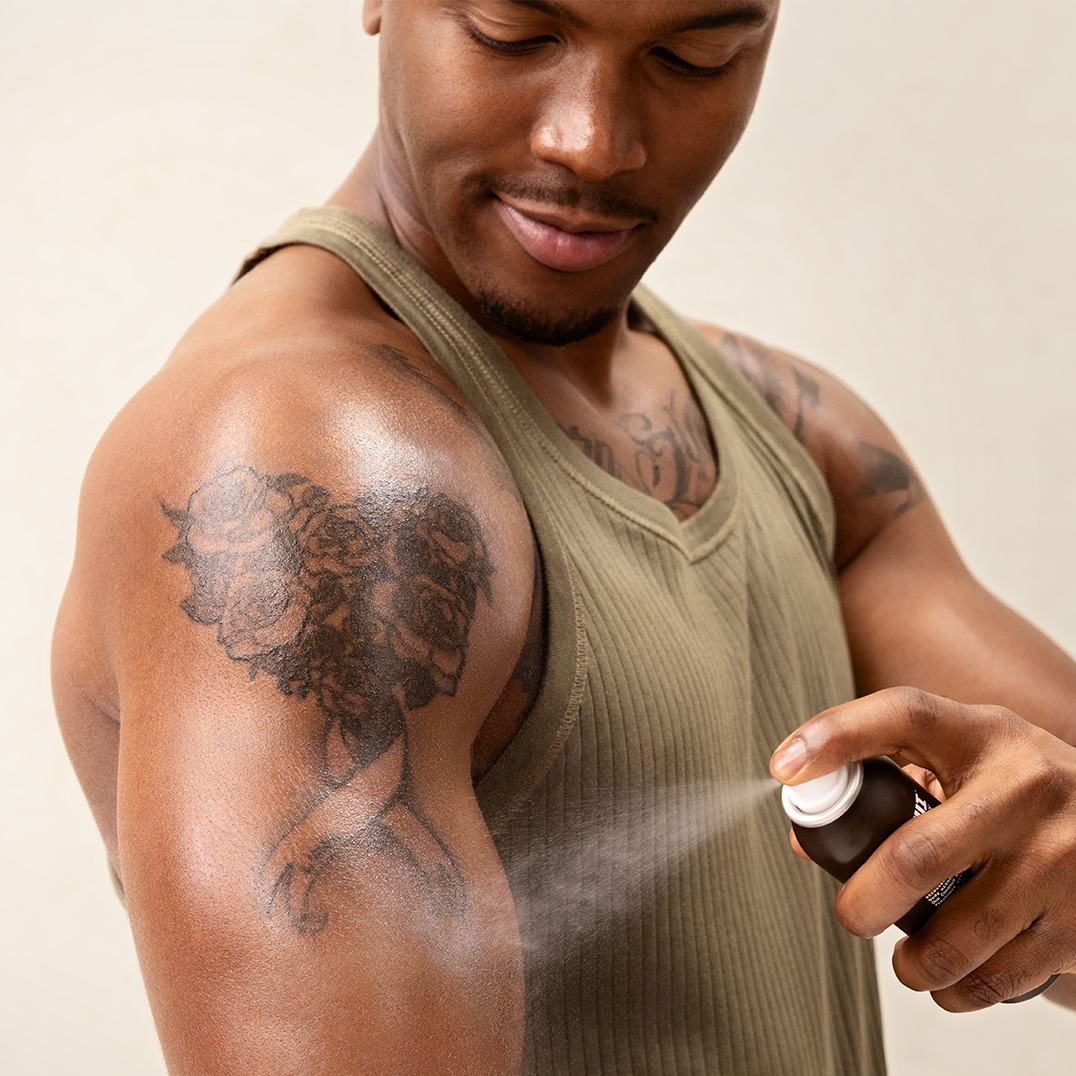 Man applying a PAPATUI Tattoo Spray product to his arm tattoos against a neutral background