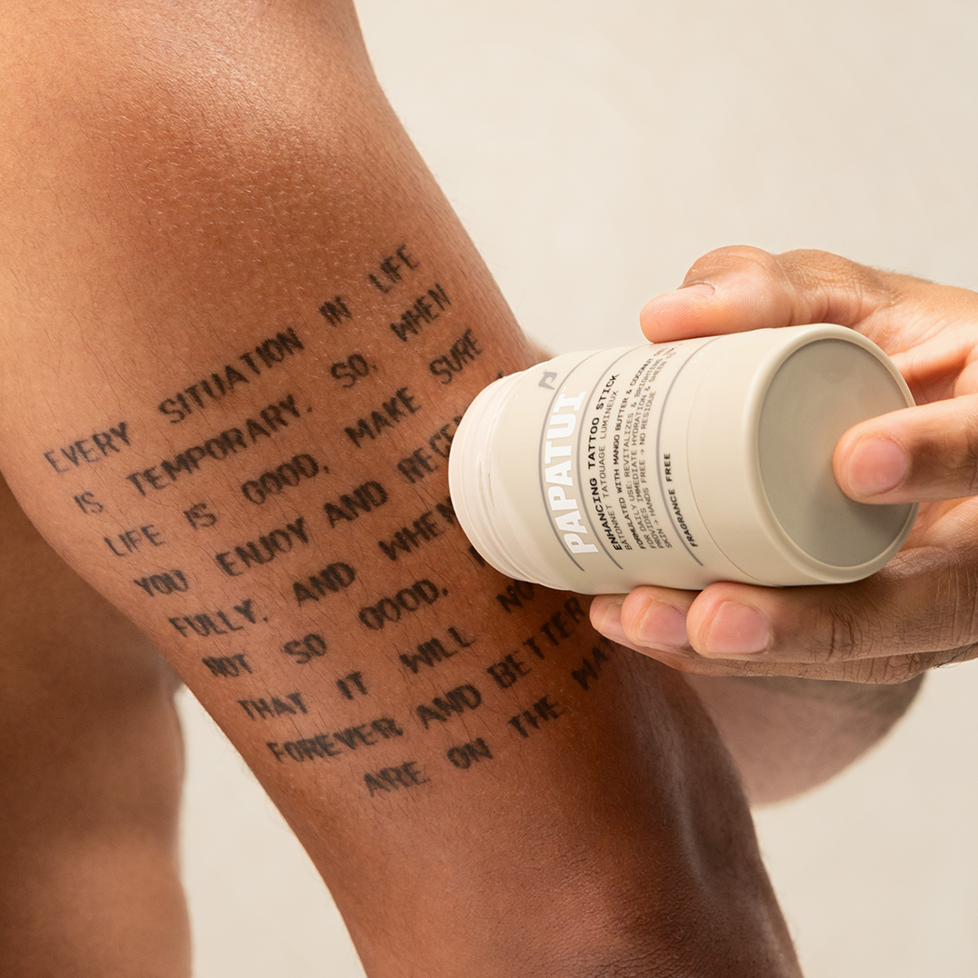 Person applying PAPATUI Enhancing Tattoo Stick to arm tattoo against a neutral background