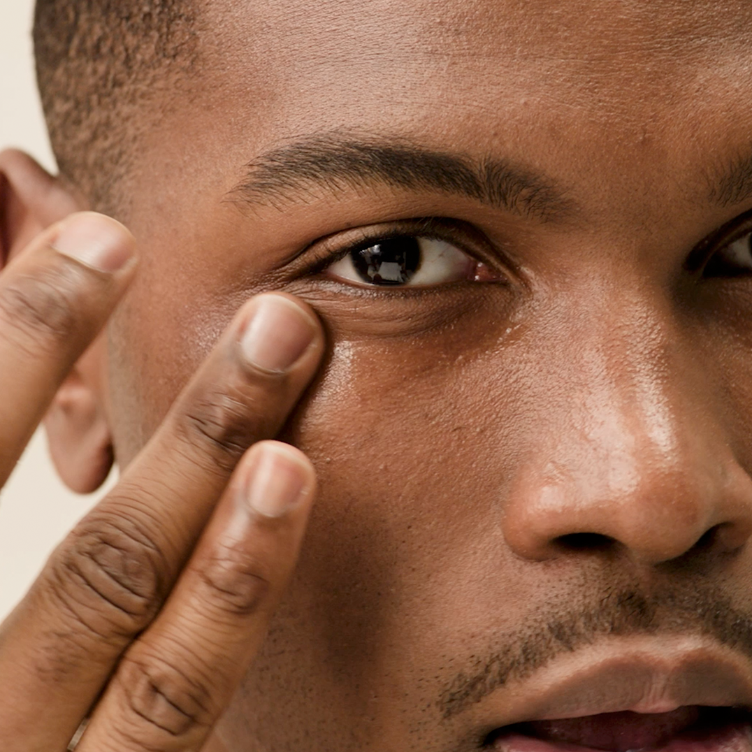 Close-up of a person applying PAPATUI Awakening Eye Gel to their eye with a finger against a neutral background