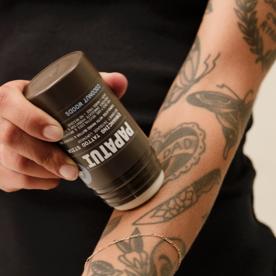 Person applying PAPATUI Enhancing Tattoo Stick to arm tattoo against a neutral background