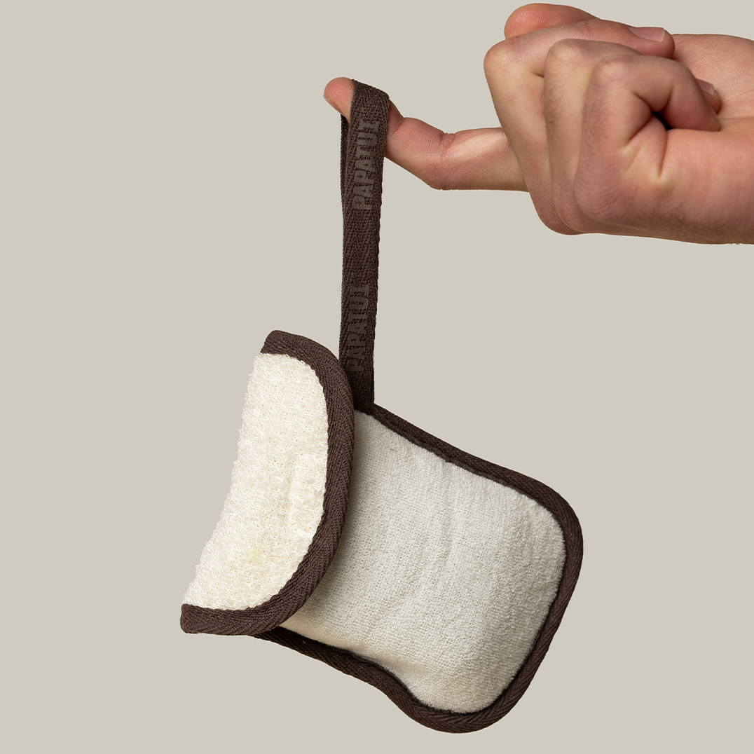 Hand holding PAPATUI Exfoliating Body Scrubber and Big Bar Soap by the handle against a neutral background
