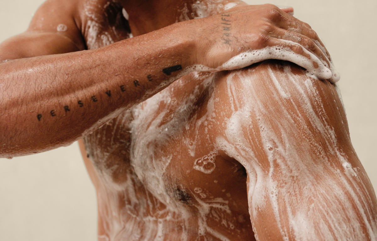 Person applying soap to their skin against a neutral background