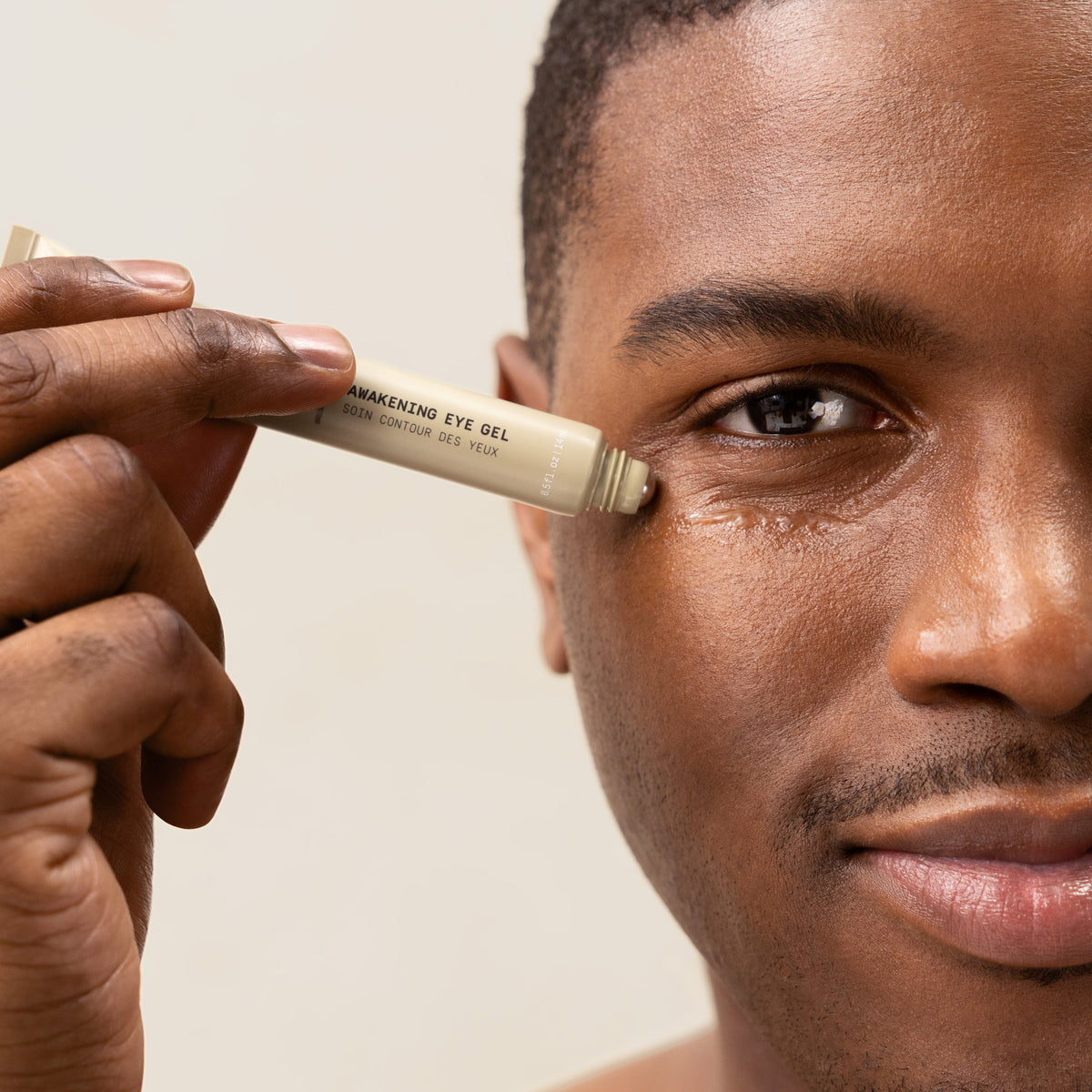 A close-up of a man applying PAPATUI Awakening Eye Gel to his under-eye against a neutral background