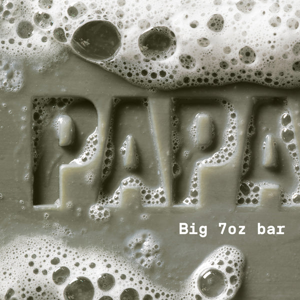 PAPATUI™ Sandalwood Suede Enriching Big Bar Soap 7oz hardworking and hydrating mens bar soap rich lather. Featuring Vitamin B3, mango butter, avocado oil, and ceramides for deep moisture and cleansing. The image shows a close-up of the embossed "PAPATUI" logo covered in foamy bubbles, emphasizing its luxurious, nourishing formula.