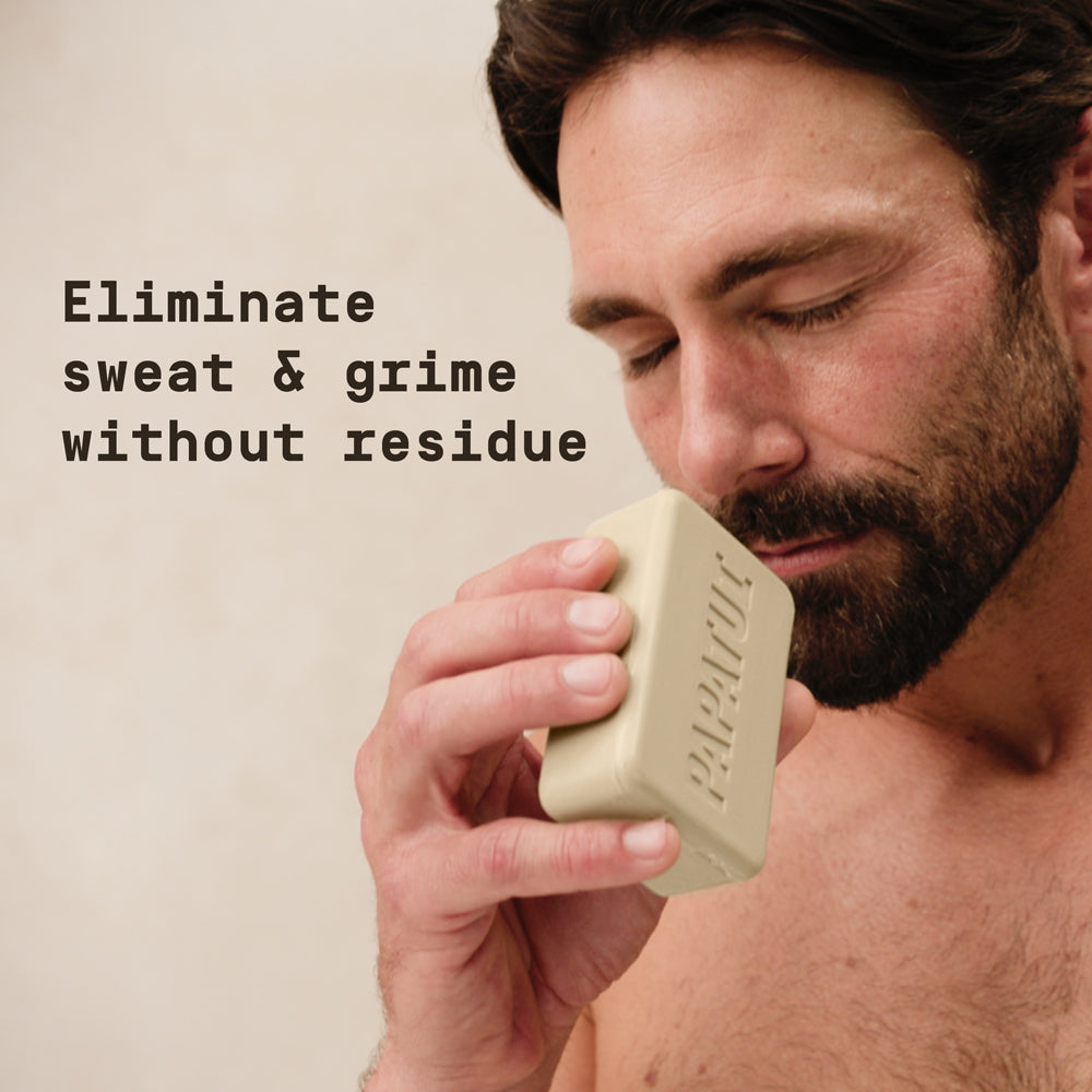 Man smelling a bar of PAPATUI soap against a neutral background with text overlay that reads "Eliminate sweat & grime without residue"