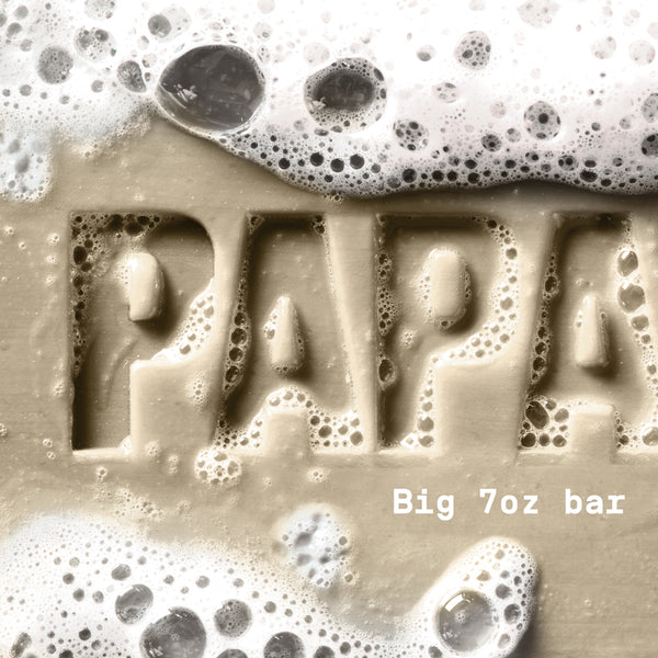 PAPATUI™ Vanilla Shea Enriching Big Bar Soap 7oz hardworking and hydrating mens bar soap rich lather. Featuring Vitamin B3, mango butter, avocado oil, and ceramides for deep moisture and cleansing. The image shows a close-up of the embossed "PAPATUI" logo covered in foamy bubbles, emphasizing its luxurious, nourishing formula.
