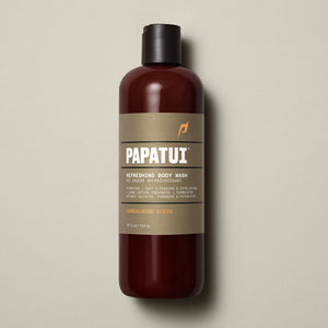 PAPATUI™ Refreshing Body Wash 18 fl oz in Sandalwood Suede scent. The product is presented in an amber bottle with a beige minimalist label and black flip cap. Key label highlights include hydrating and exfoliating formula with long-lasting freshness. Claims sulfate-free, paraben-free, phthalate-free formulation. Neutral beige background.