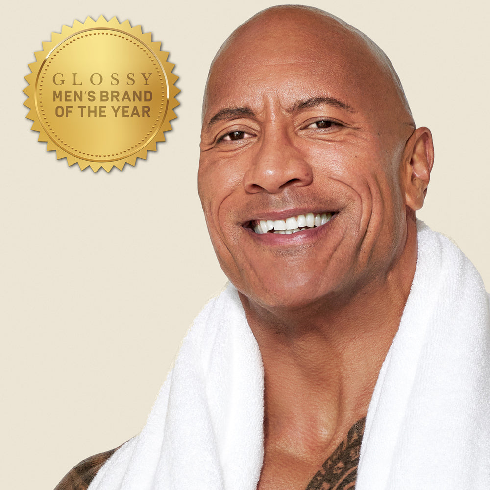 Dwayne "The Rock" Johnson with a white towel draped over his shoulders against a neutral background with a gold award badge reading Men's Brand of the Year"