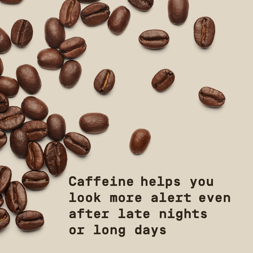 Coffee beans scattered on a neutral background with text overlay that reads "Caffeine helps you look more alert even after late nights or long days"