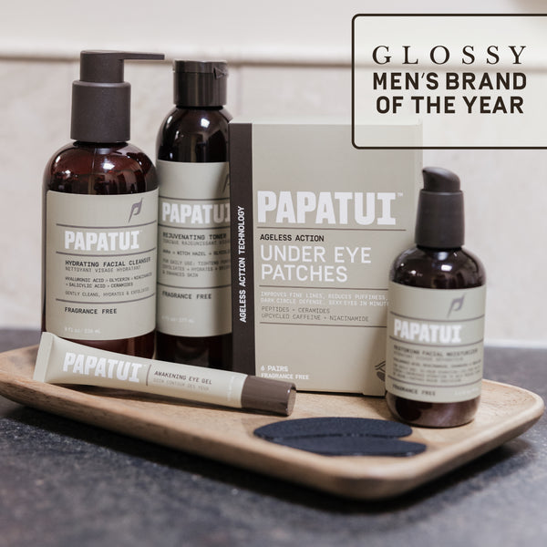 PAPATUI™A premium men’s skincare lineup displayed on a wooden tray, featuring the Hydrating Facial Cleanser, Rejuvenating Toner, Restoring Facial Moisturizer, Awakening Eye Gel, and Ageless Action Under Eye Patches. A "Glossy Men's Brand of the Year" badge highlights the brand’s excellence.