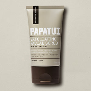 PAPATUI™ Exfoliating Mens Facial Scrub unscented 4oz tube. The packaging features a beige and brown design with bold white text. It highlights key ingredients like volcanic ash, peptides, niacinamide, and hyaluronic acid, promoting exfoliation, brightening, and minimizing fine lines and pores. The label also states ‘Fragrance Free’ and ‘Ageless Action Technology.