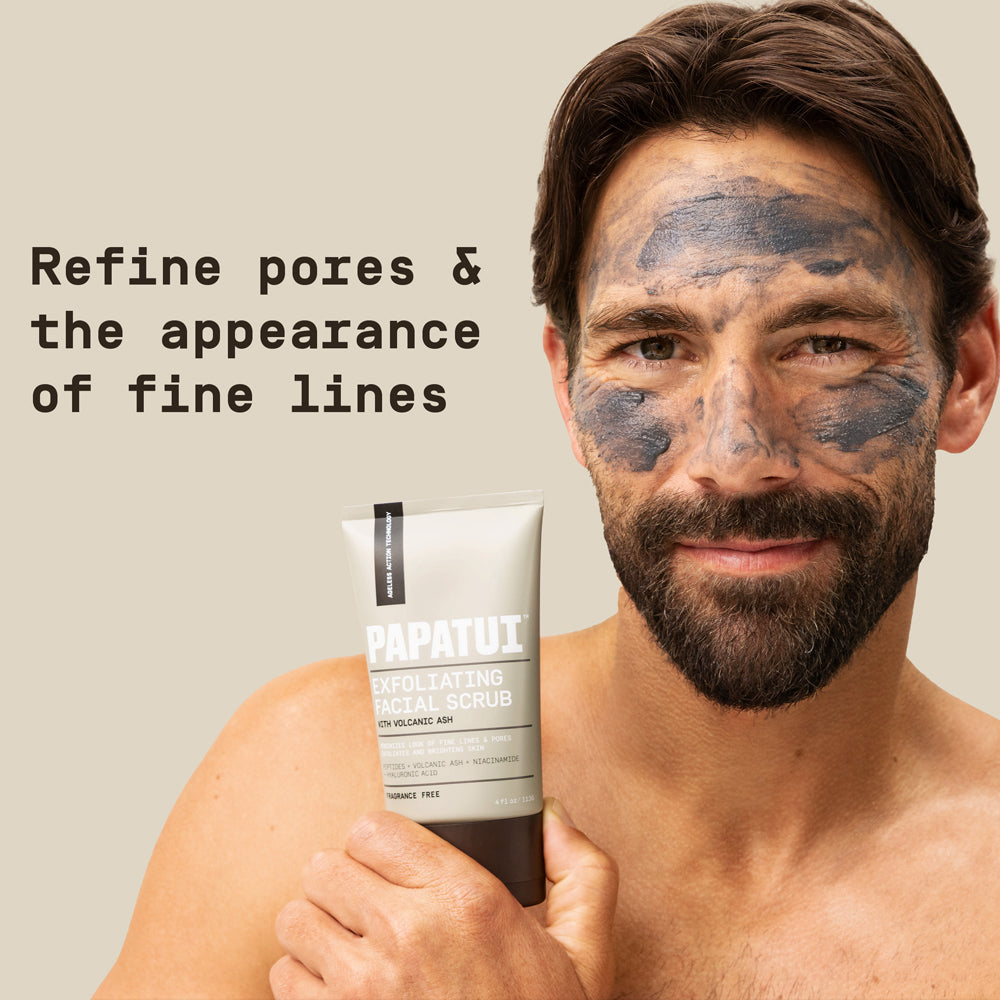 Man holding PAPATUI Men’s Exfoliating Facial Scrub with PAPATUI Men’s Exfoliating Facial Scrub on his face against  a neutral background with text overlay that reads "Refine pores & the appearance of fine lines"