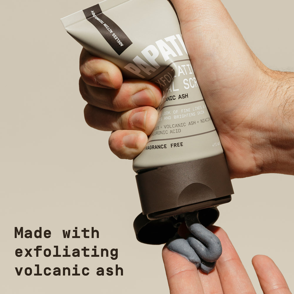 Man squeezing PAPATUI Men’s Exfoliating Facial Scrub into his hand against a neutral background with text overlay that reads "Made with exfoliating volcanic ash"