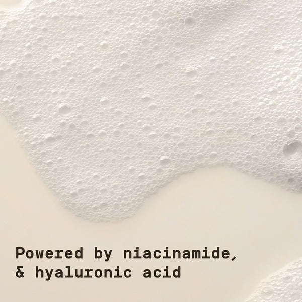 Text 'Powered by niacinamide & hyaluronic acid' on a white background with face cleanser bubbles on the surface.