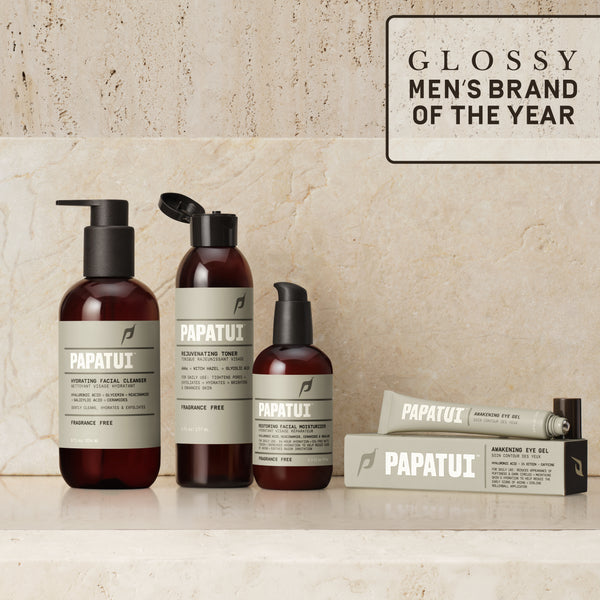 PAPATUI™A premium men’s skincare lineup displayed on marble surface, featuring the Hydrating Facial Cleanser, Rejuvenating Toner, Restoring Facial Moisturizer, Awakening Eye Gel, and Ageless Action Under Eye Patches. A "Glossy Men's Brand of the Year" badge highlights the brand’s excellence.
