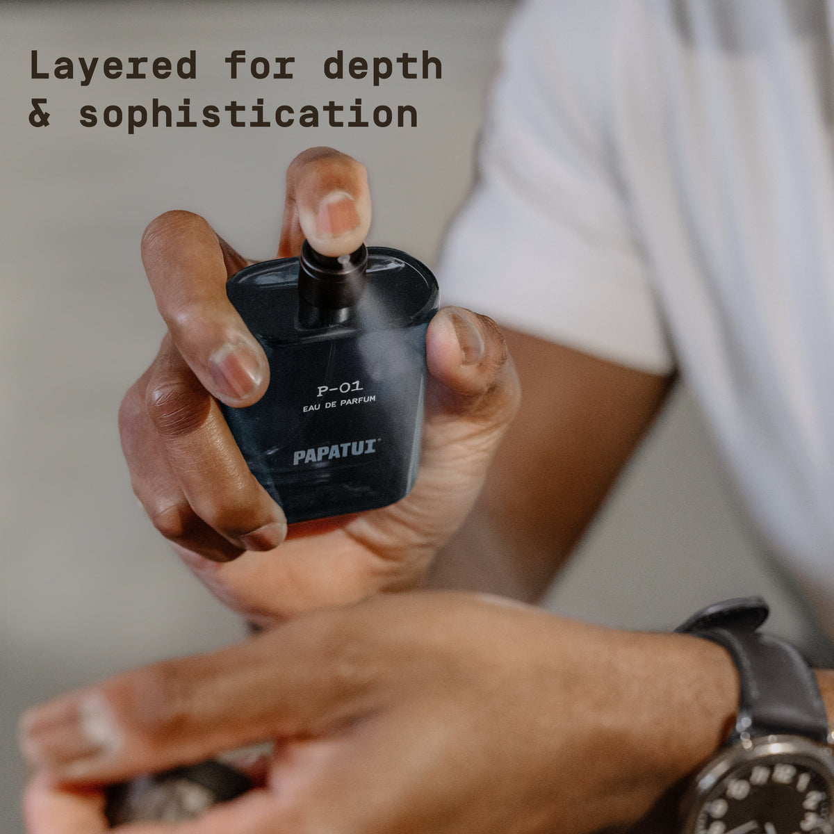 Man spraying a blue cologne bottle labeled 'P-01 Eau de Parfum' by 'PAPATUI' with text overlay reading "Layered for depth & sophistication"
