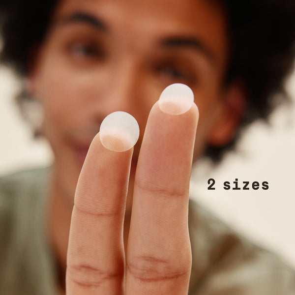 Close-up of a person's hand holding two small white objects with text '2 sizes' on a blurred background. - Papatui Pimple Patches
