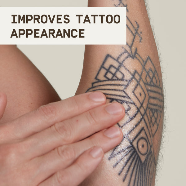 Close-up image of a person applying PAPATUI™ Enhancing Tattoo Balm 2oz to a geometric black tattoo on their forearm. The skin appears hydrated and slightly glossy, highlighting the balm’s moisturizing effect. A bold text overlay reads, 'Improves Tattoo Appearance,' emphasizing the product's benefits. The neutral background keeps the focus on the tattoo and application process, reinforcing the balm’s role in enhancing vibrancy and maintaining tattoo longevity.