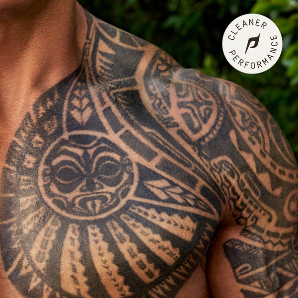 Close-up of Dwayne Johnson’s chest and shoulder tribal tattoo appears vibrant and well-defined, highlighting deep blacks and sharp details. The background features lush green foliage, adding a natural contrast to the tattoo. A circular badge in the top right corner reads 'Cleaner Performance,' reinforcing the effectiveness of PAPATUI™ Enhancing Tattoo Balm 2oz in maintaining tattoo vibrancy and clarity.